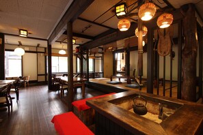 Et traditionelt japansk restaurantmiljø med trægulv, tatamimåtter, lave borde og hængende papirlanterner.