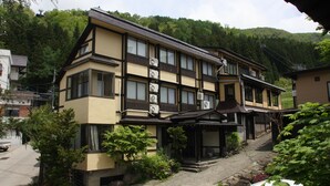 Un edificio de estilo japonés tradicional con varias unidades de aire acondicionado, un acceso empedrado y un pequeño jardín con rocas y plantas.