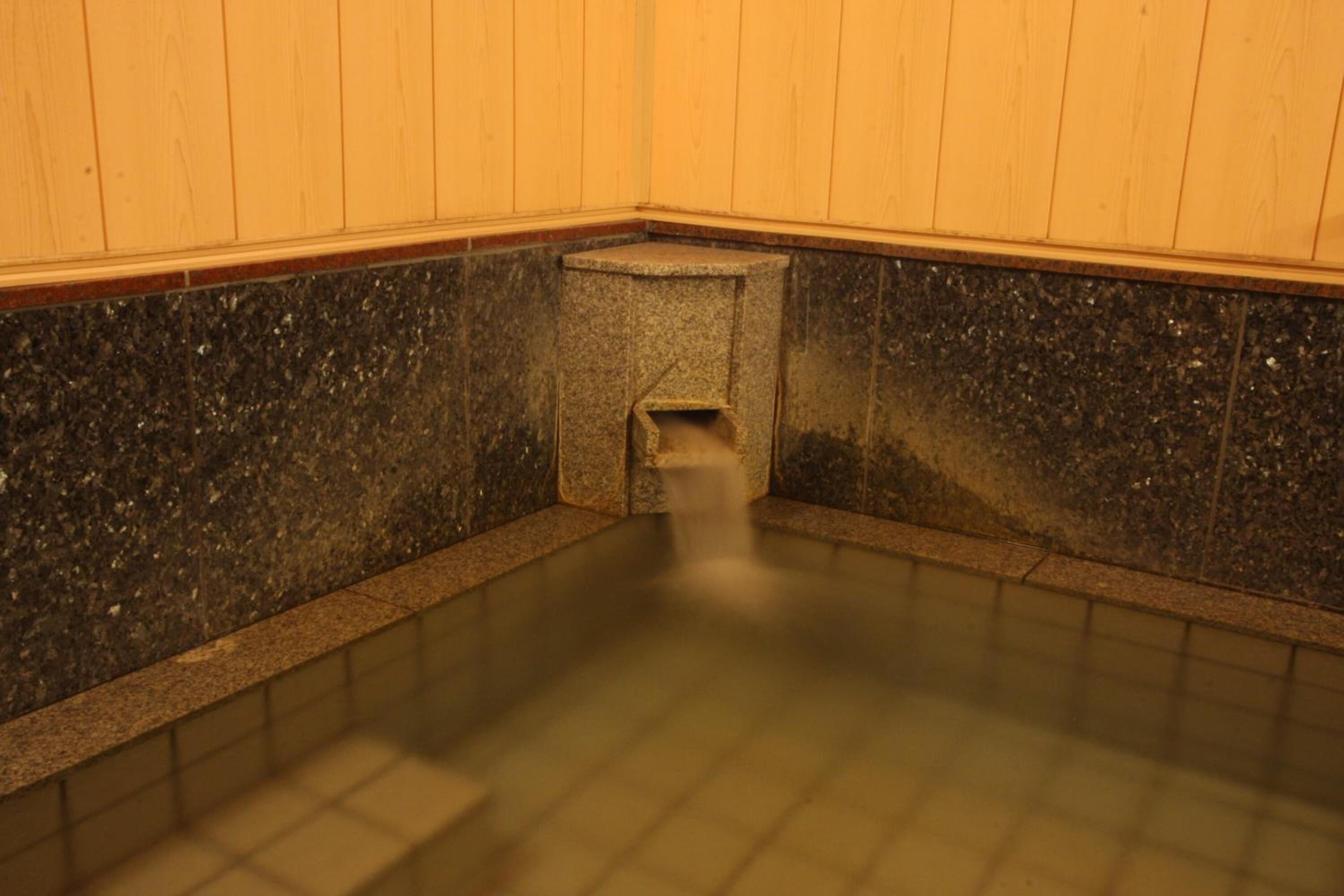 A small stone hot tub with a tiled floor and wooden walls.