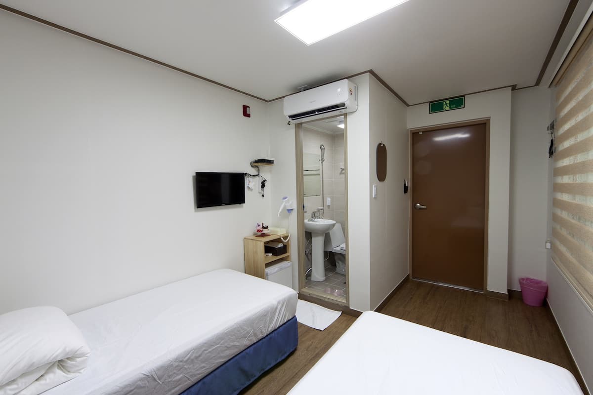 A hotel room with two beds, a bathroom, and an air conditioning unit.