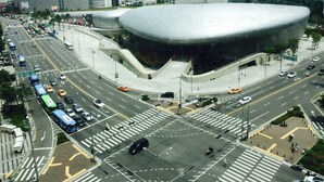 A modern building with a unique curved roof, surrounded by a busy intersection with multiple lanes and vehicles. - Charim Guesthouse (Seoul)