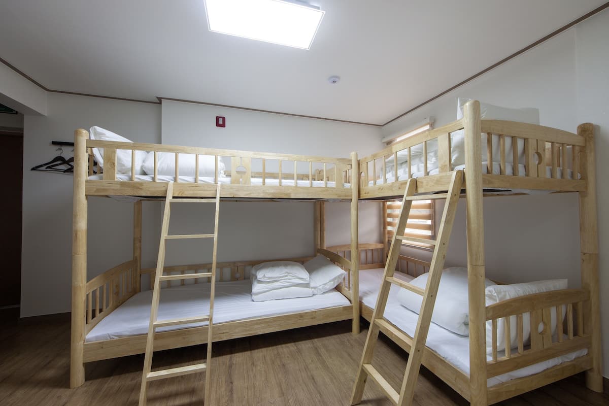 A bunk bed room with wooden frames, white bedding, and a ceiling light.