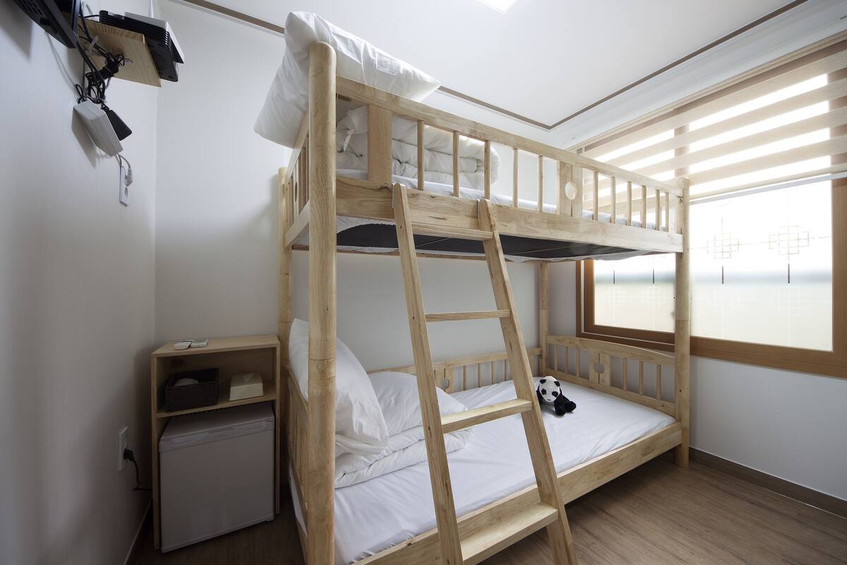 A bunk bed with a ladder, a small desk, and a window with blinds.