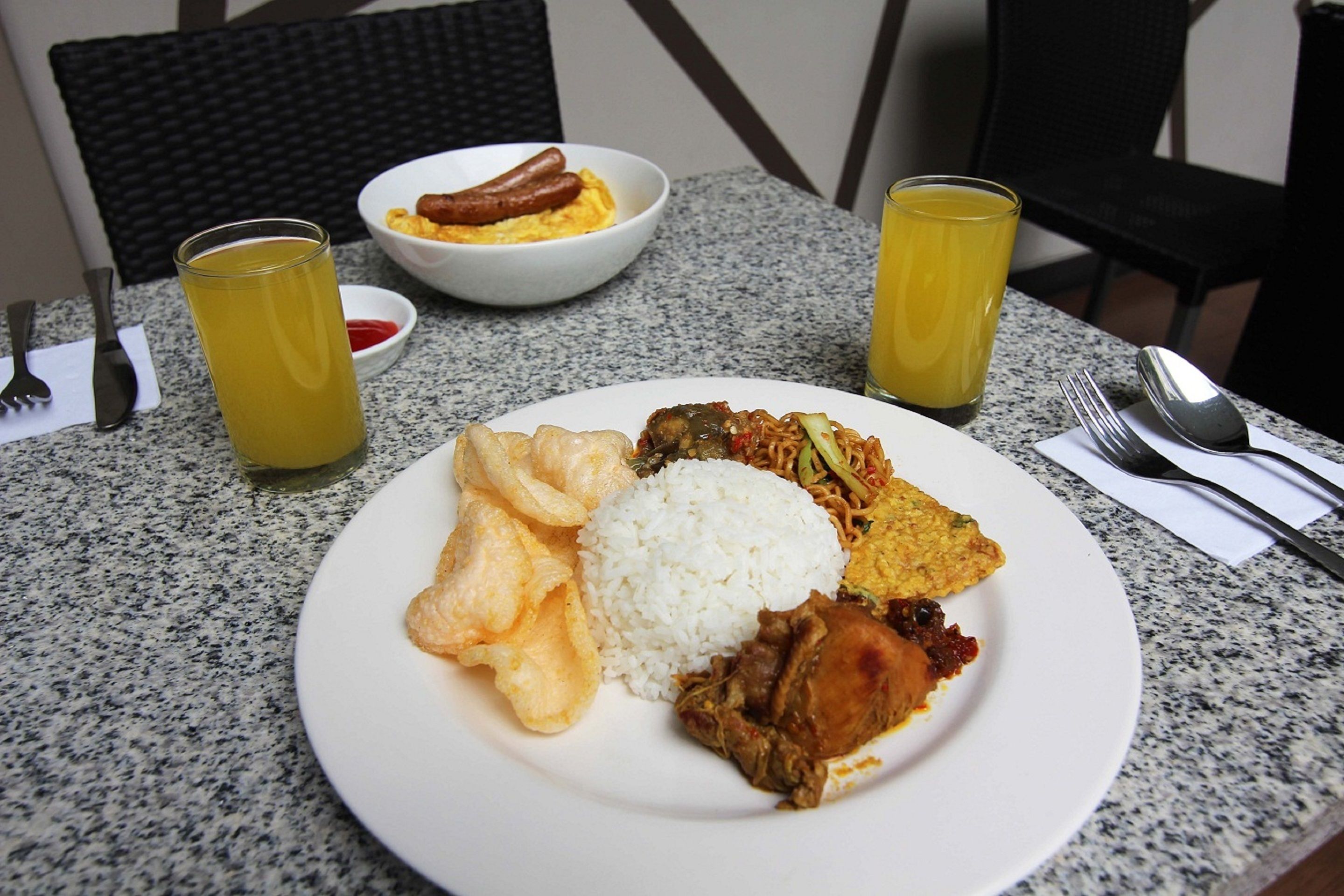 Prato de comida com arroz, carne e frituras, acompanhado de um tacho de enchidos e um copo de suco.
