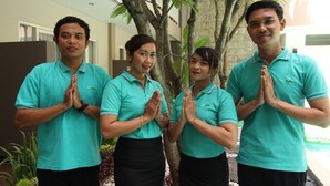 Quatre personnes portant des chemises turquoise, debout en rang, les mains jointes dans un geste de salutation ou de prière.