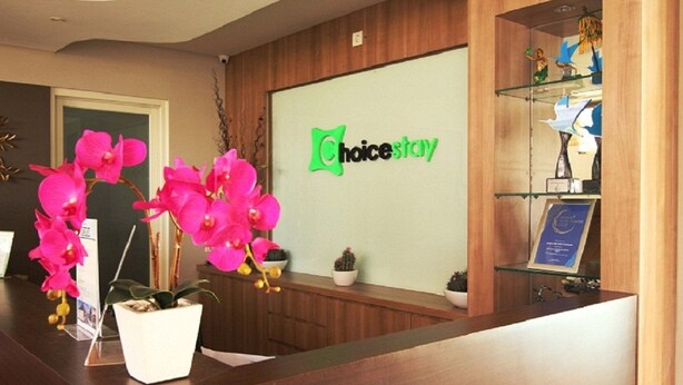 Un espace d’accueil comprenant un comptoir de réception en bois, une vitrine et une enseigne fixée au mur portant l’inscription « ChoiceStay ».