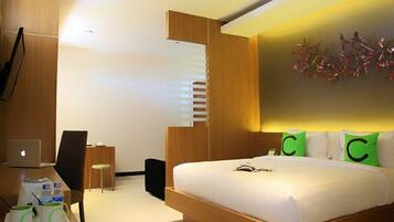 A modern hotel room with a wooden bed, a desk with a laptop, a chair, and a small table with cups and a book.