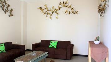 A living room with two brown sofas, a glass coffee table, and a small wooden side table with a plant.