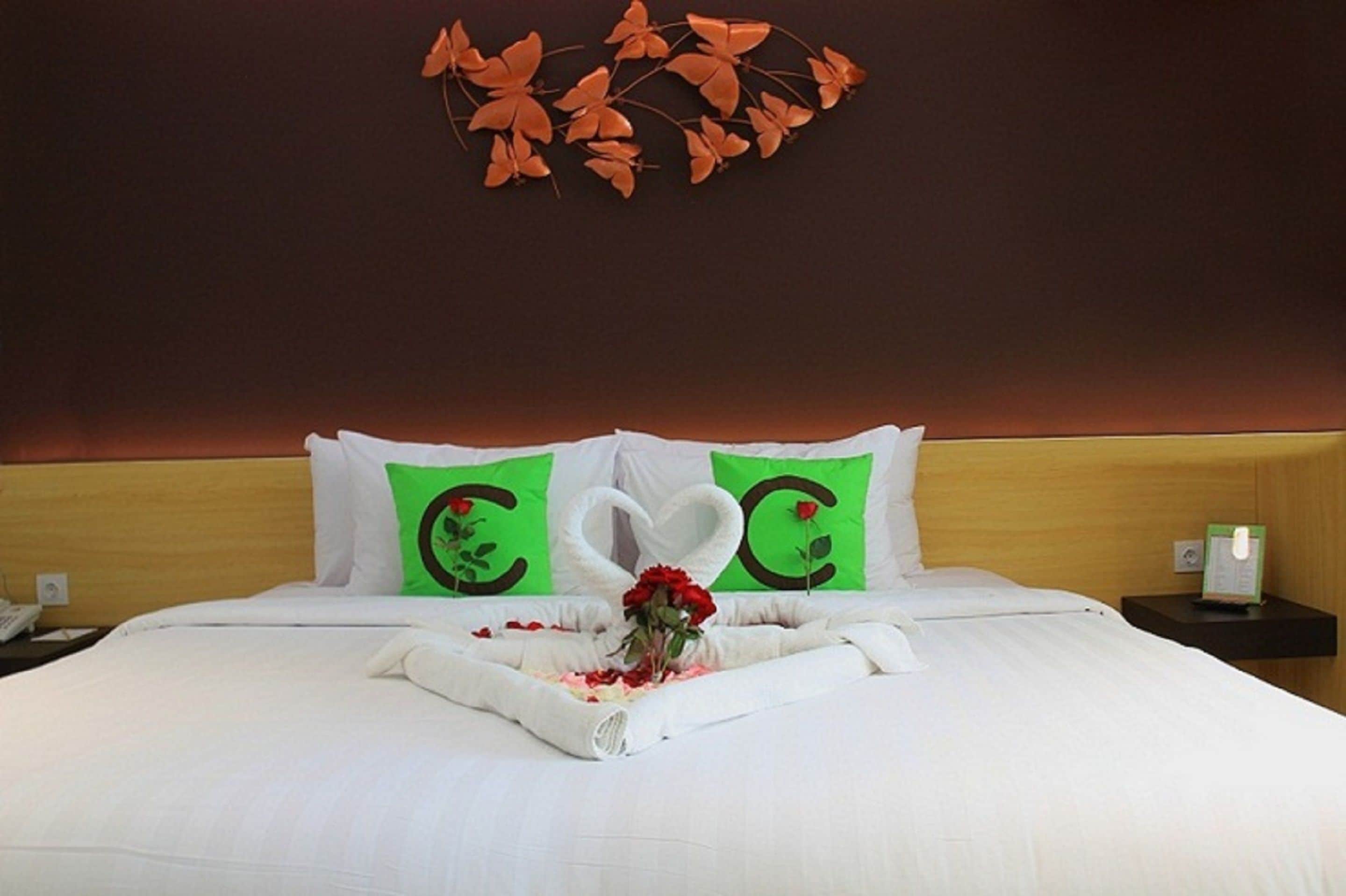 Una camera d'albergo con un letto rifatto, cuscini verdi con un motivo a cuore e una decorazione a parete con foglie arancioni.