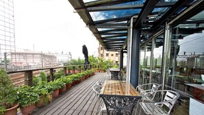 A rooftop terrace with a wooden deck, potted plants, metal chairs, and a glass railing. - Hotel Les Champs Jiaosi (Jiaoxi)