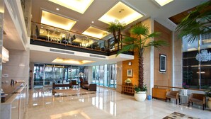 A spacious lobby with a high ceiling, a palm tree, and a seating area. - Hotel Les Champs Jiaosi (Jiaoxi)