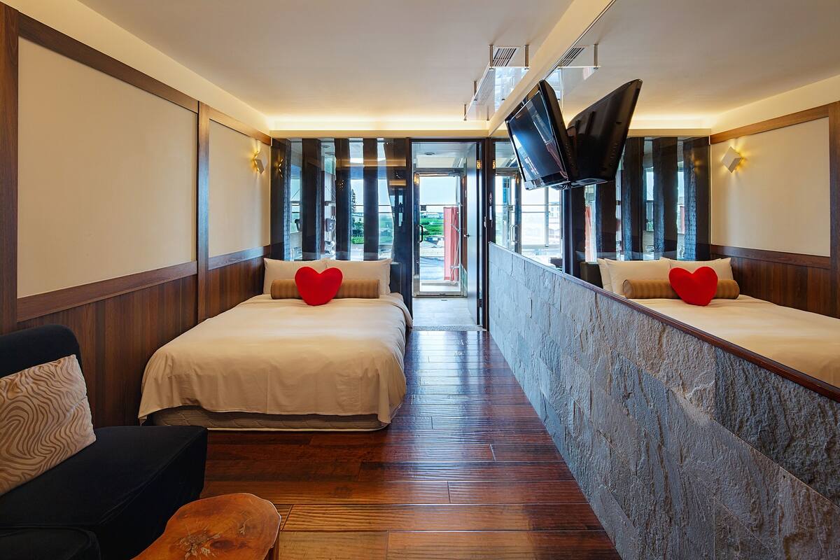 A hotel room with two beds, a TV, and a view of the outside.
