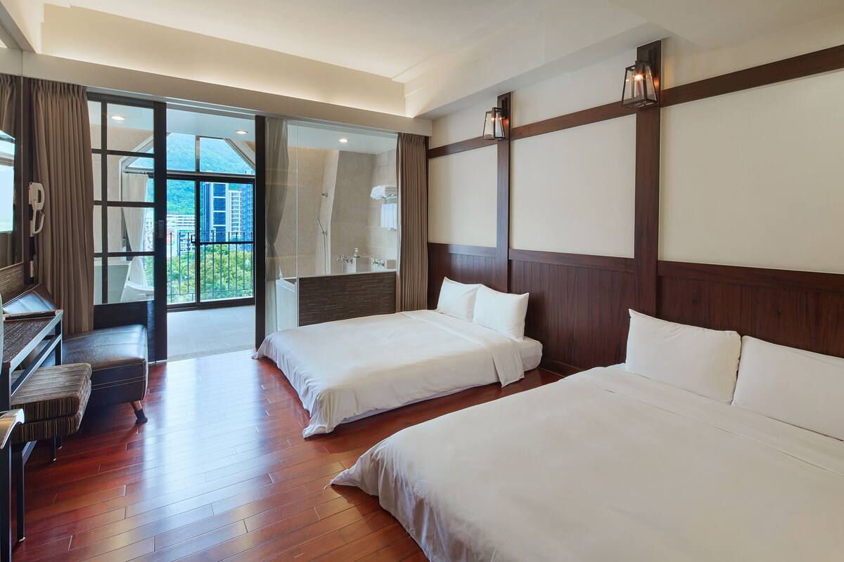 A hotel room with two beds, a desk, and a large sliding glass door leading to a balcony.