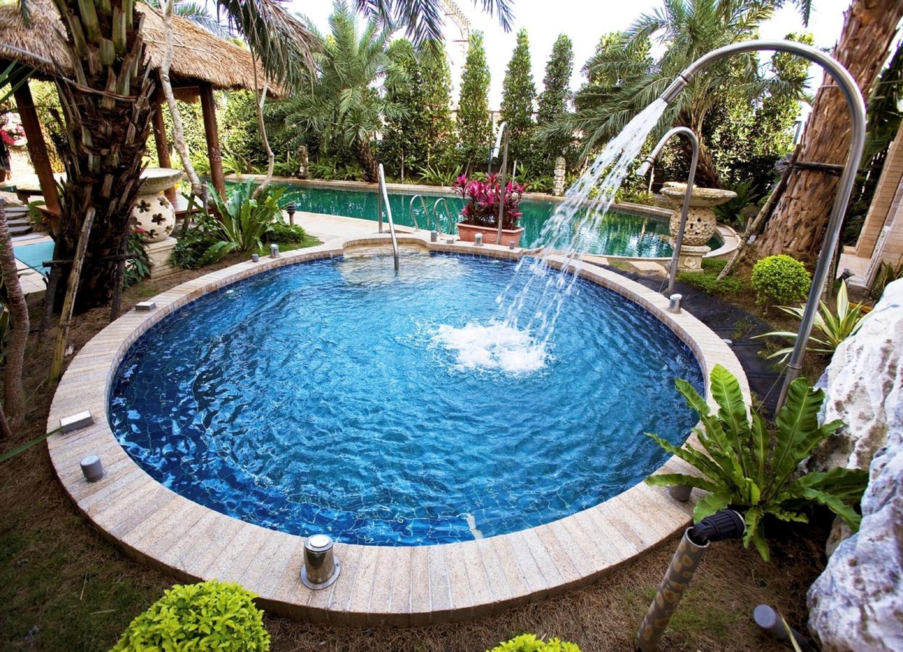 A circular swimming pool with a water fountain, surrounded by tropical plants and a thatched-roof structure.
