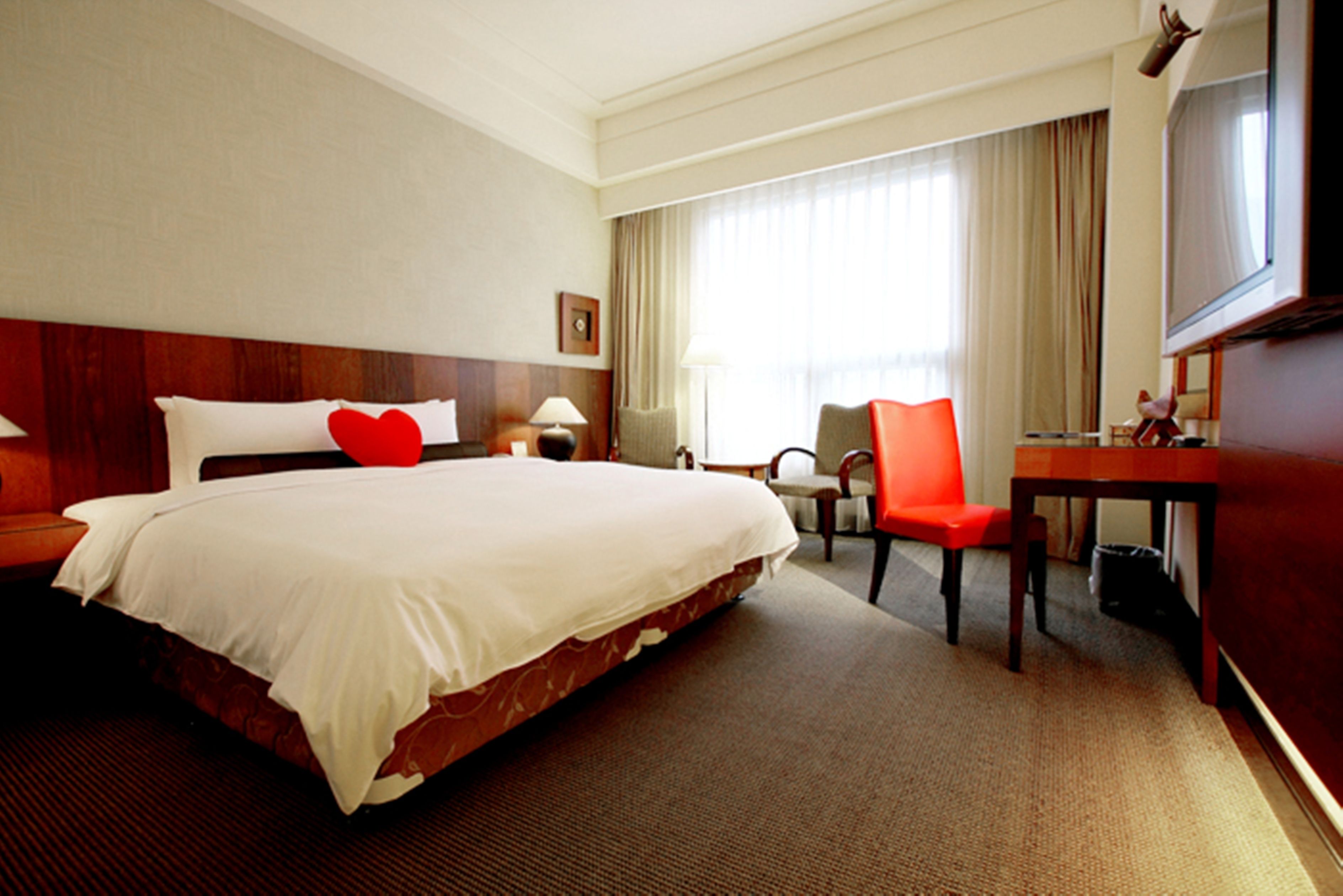 Una habitación de hotel con una cama grande, un escritorio, una silla, una lámpara y un televisor.