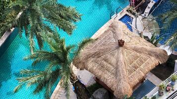 A rooftop pool with a thatched umbrella, palm trees, and potted plants.