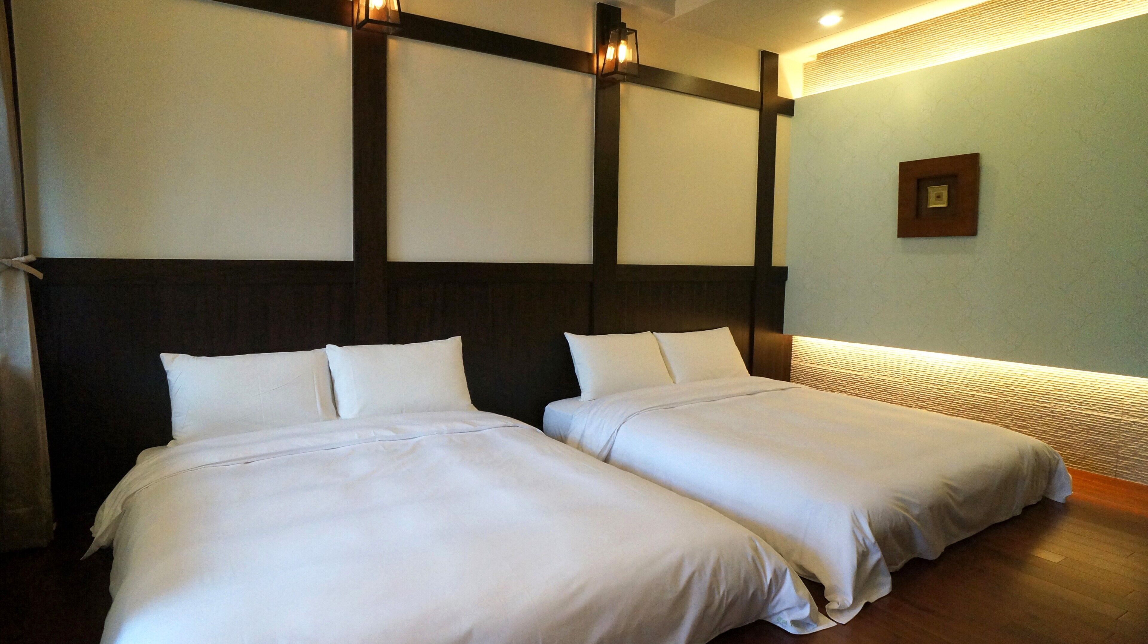 A hotel room with two beds, a dark wooden headboard, and a light-colored wall.
