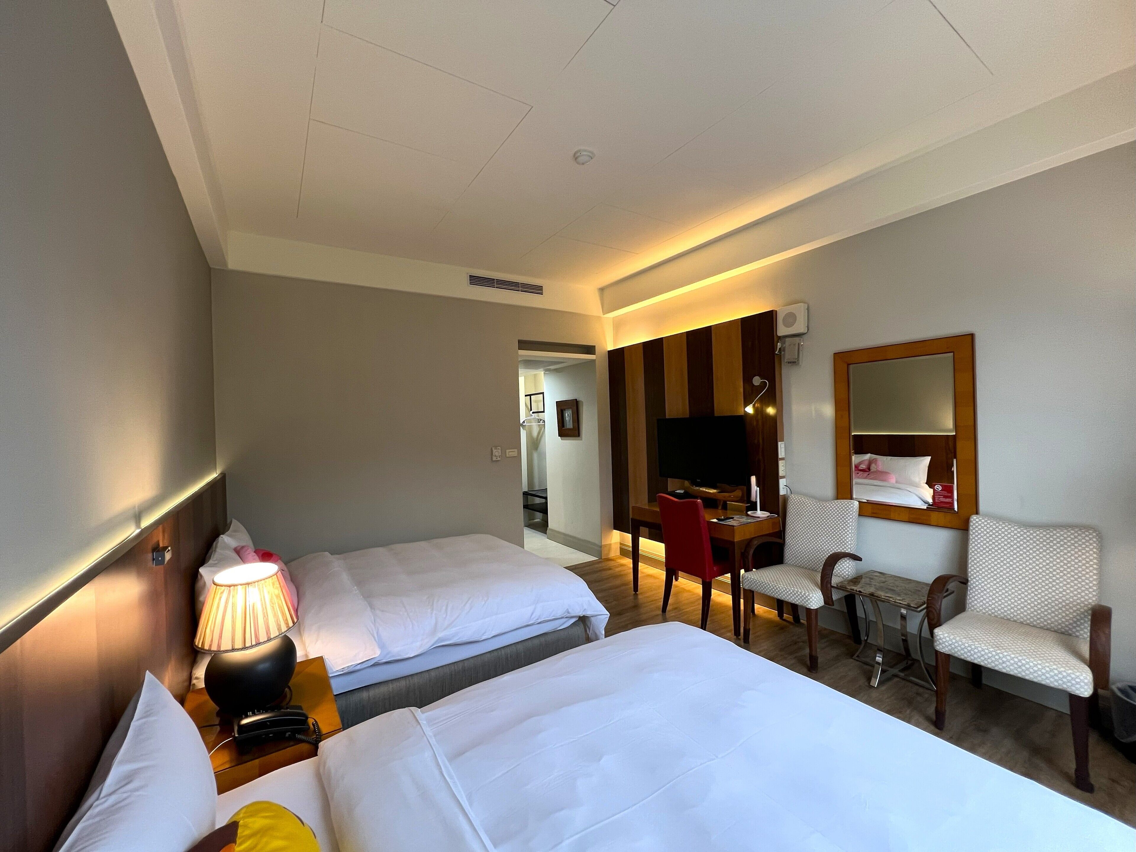 Habitación de hotel con dos camas, un escritorio, una silla, un televisor y un espejo.