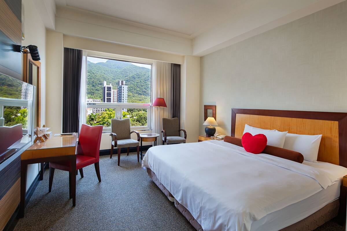 A hotel room with a large bed, a desk with a chair, a small table, and a TV.