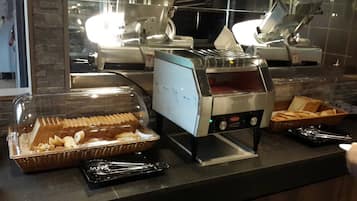 A buffet setup with a toaster oven, a covered food tray, and baskets of bread.