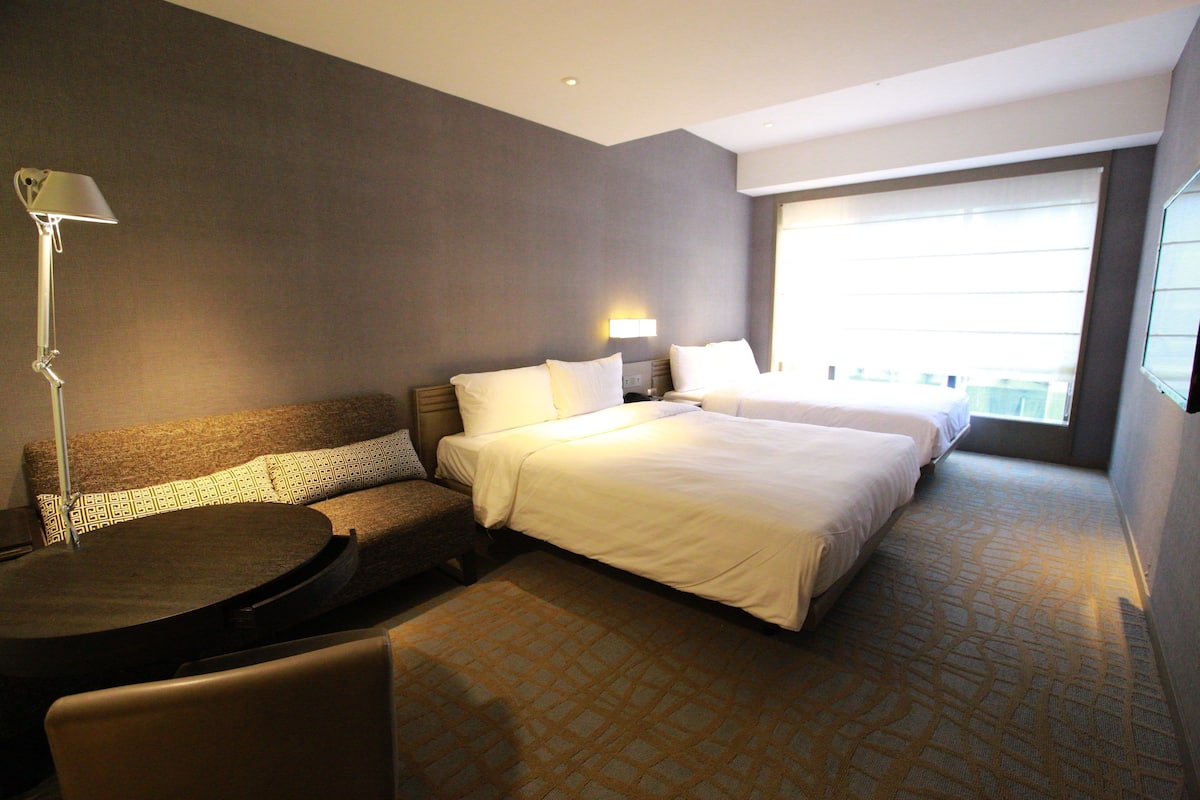 A hotel room with a large bed, a sofa, a small table, and a lamp.