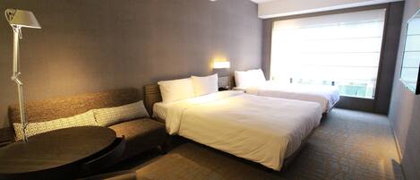 A hotel room with a large bed, a sofa, a small table, and a lamp.