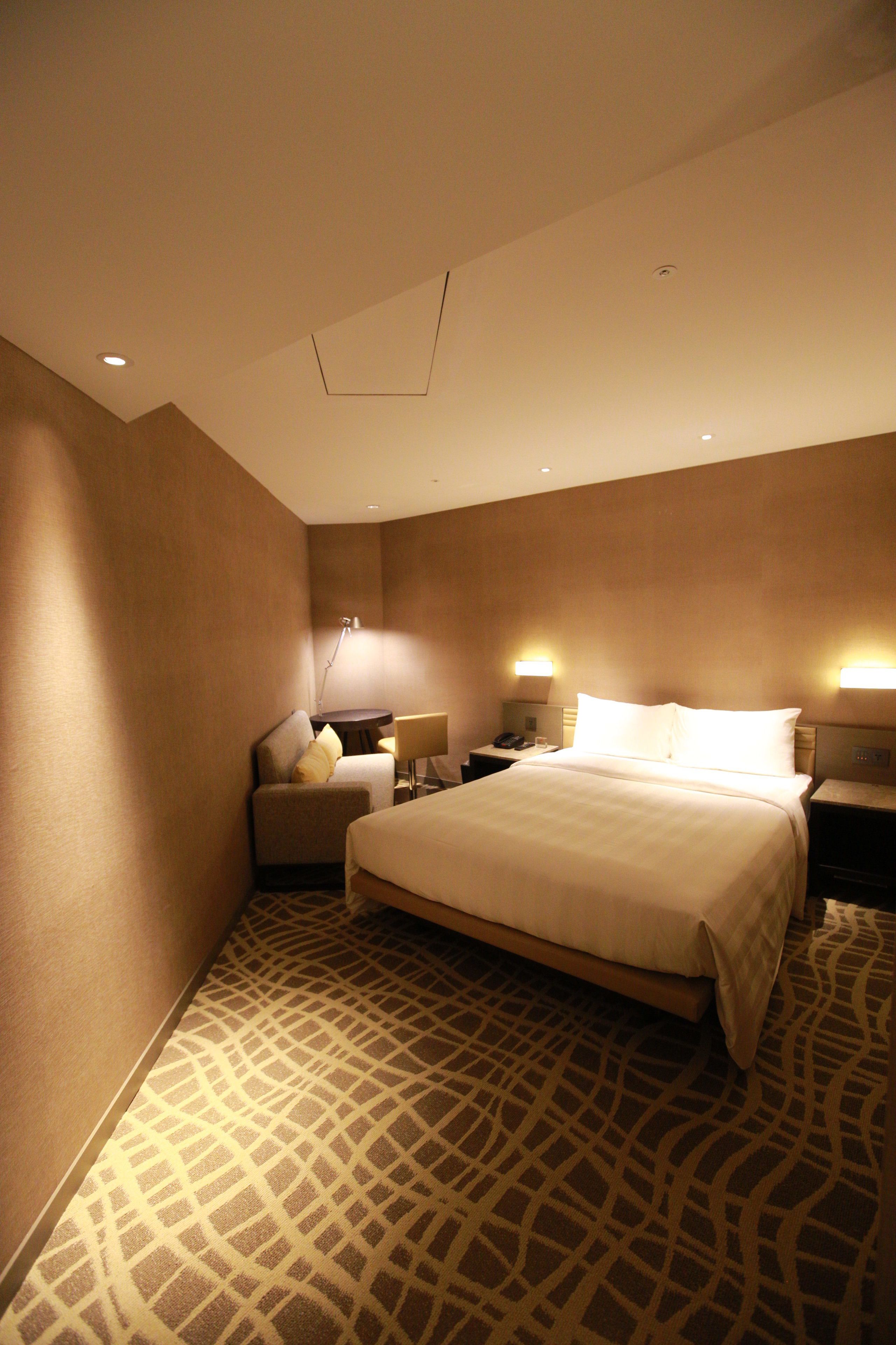 A hotel room with a large bed, a desk, a chair, and two bedside lamps.
