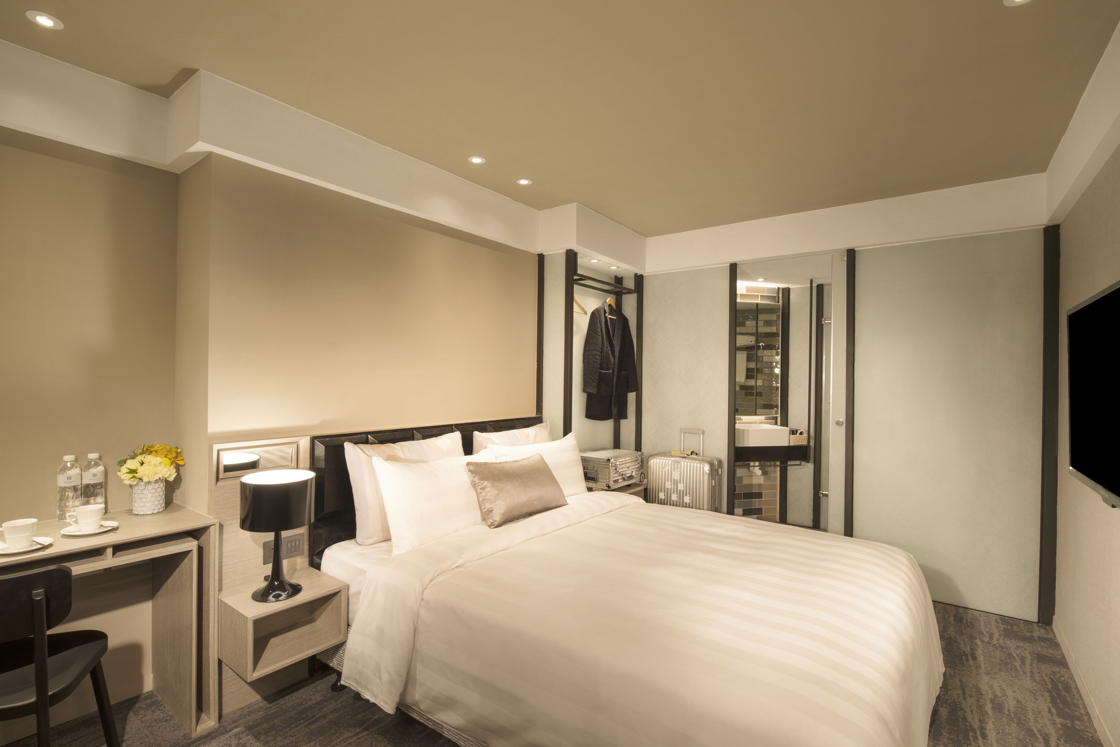 A hotel room with a bed, desk, chair, lamp, and a mirror.