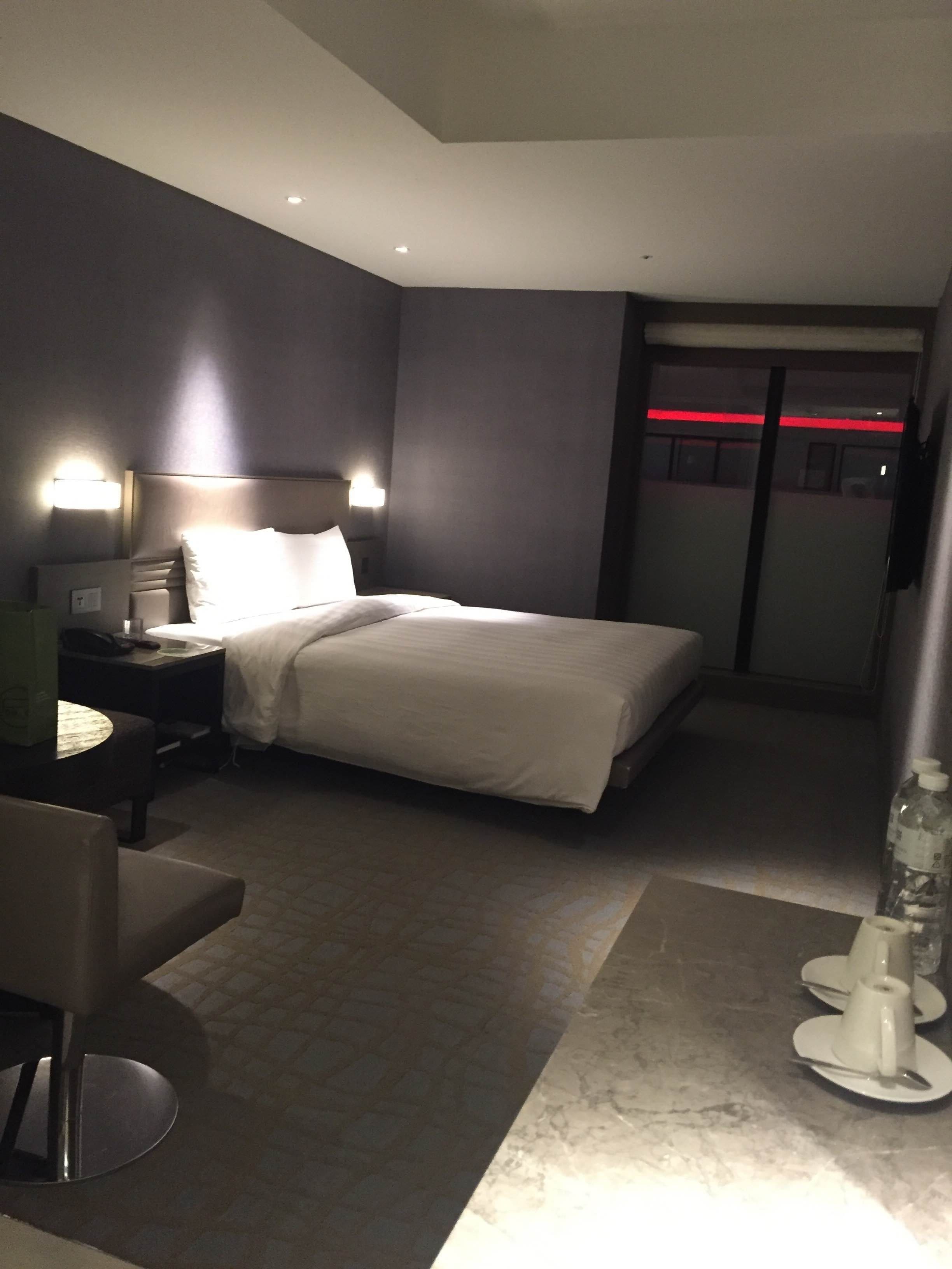 A hotel room with a bed, bedside tables, a chair, and a small table with a bottle and glasses.