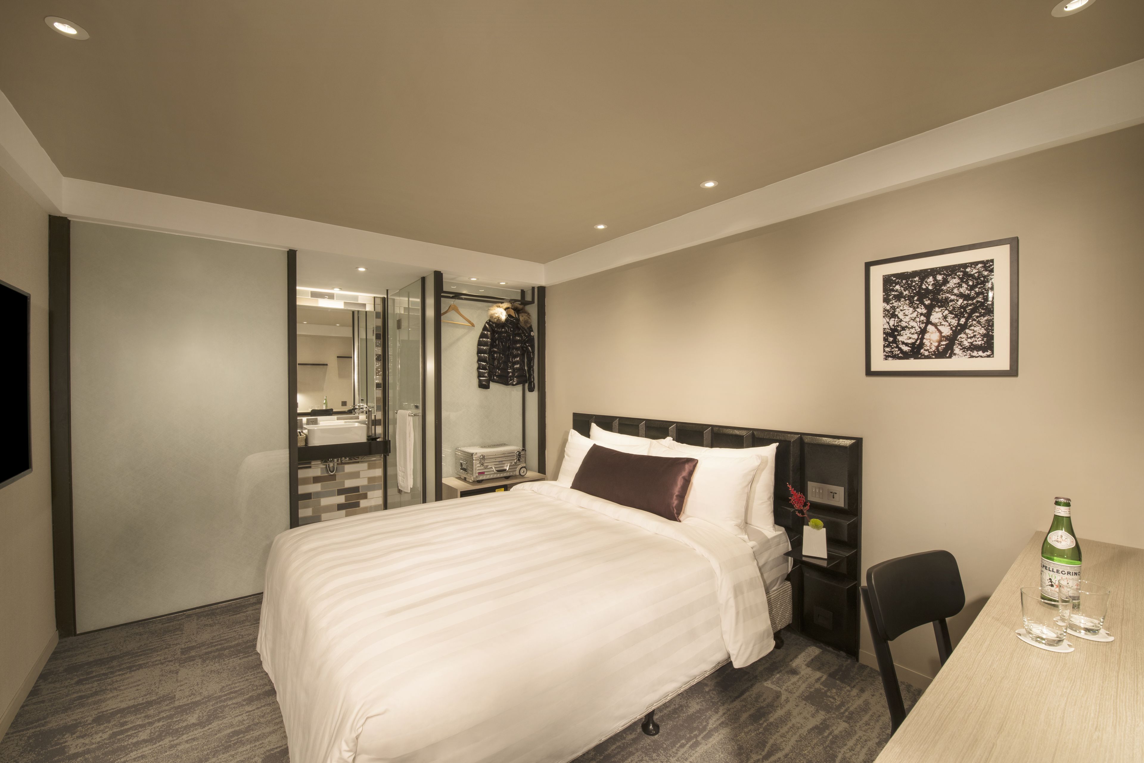 Ein modernes Hotelzimmer mit einem großen Bett, einem Schreibtisch, einem Sessel, einer Minibar und einem gerahmten Bild an der Wand.