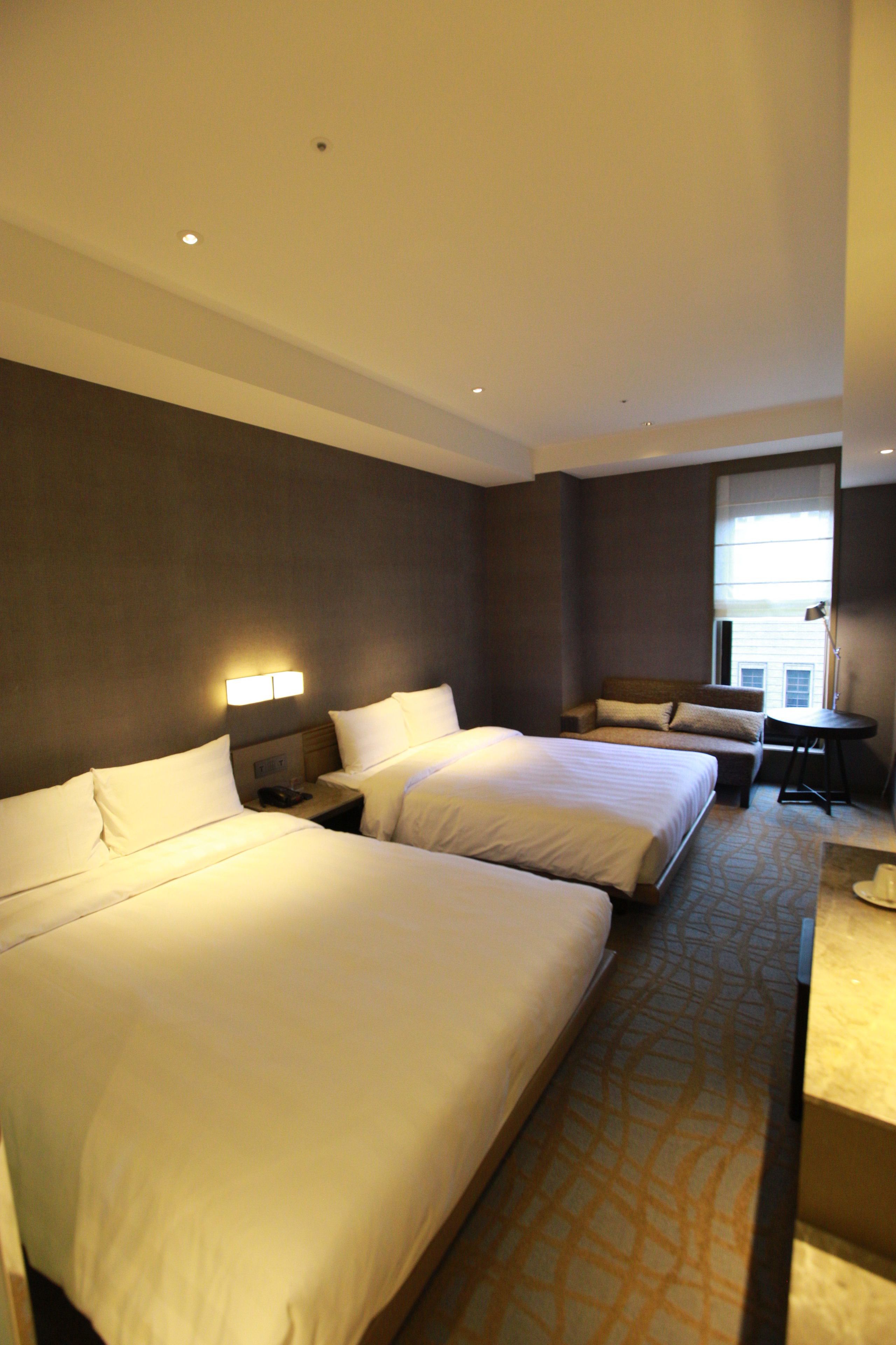A hotel room with two beds, a small table, and a chair.