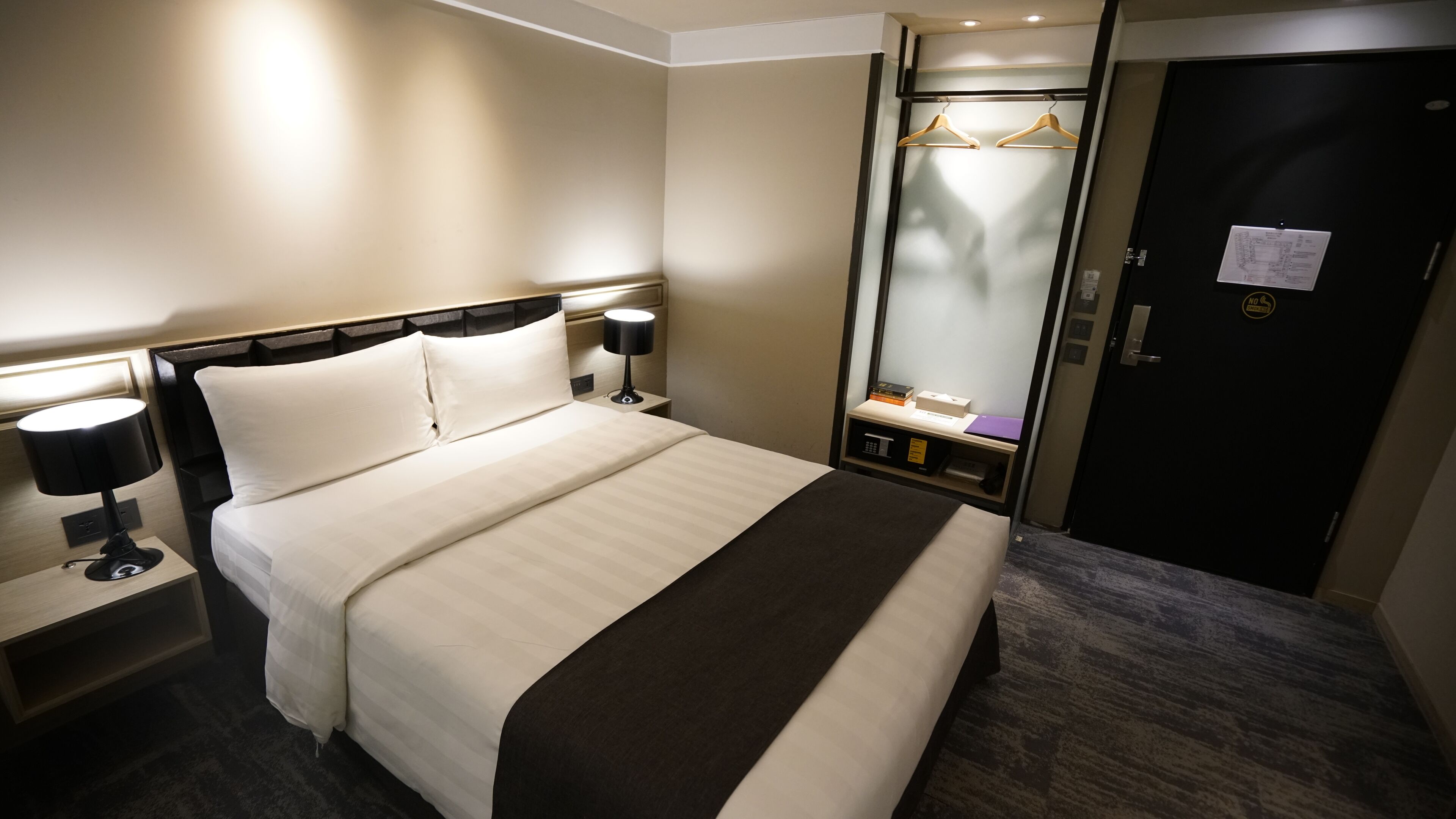 Een hotelkamer met een bed, nachtlampjes, een kledingkast en een spiegel.