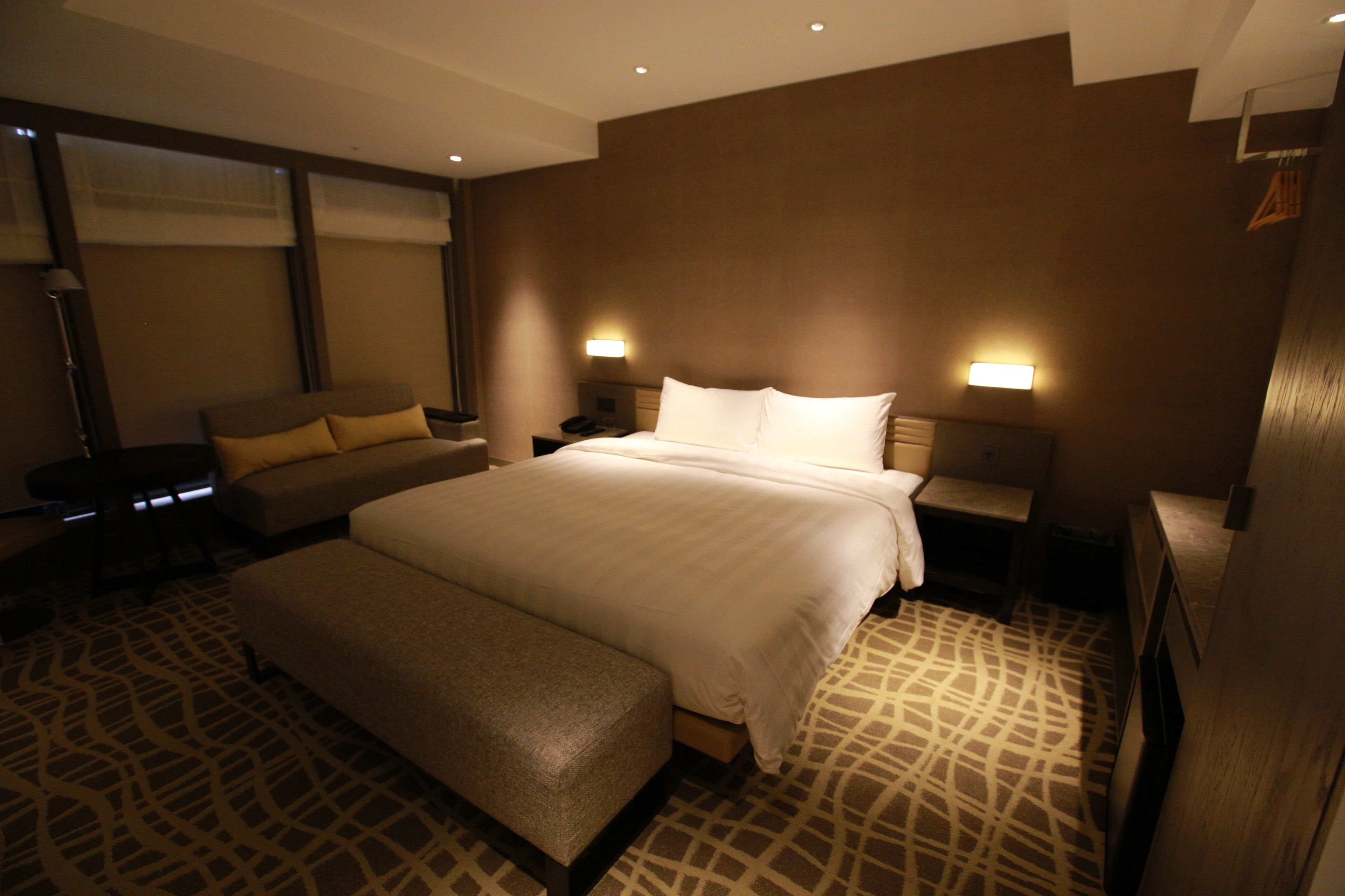 A hotel room with a large bed, a sofa, a bench, and two bedside tables with lamps.