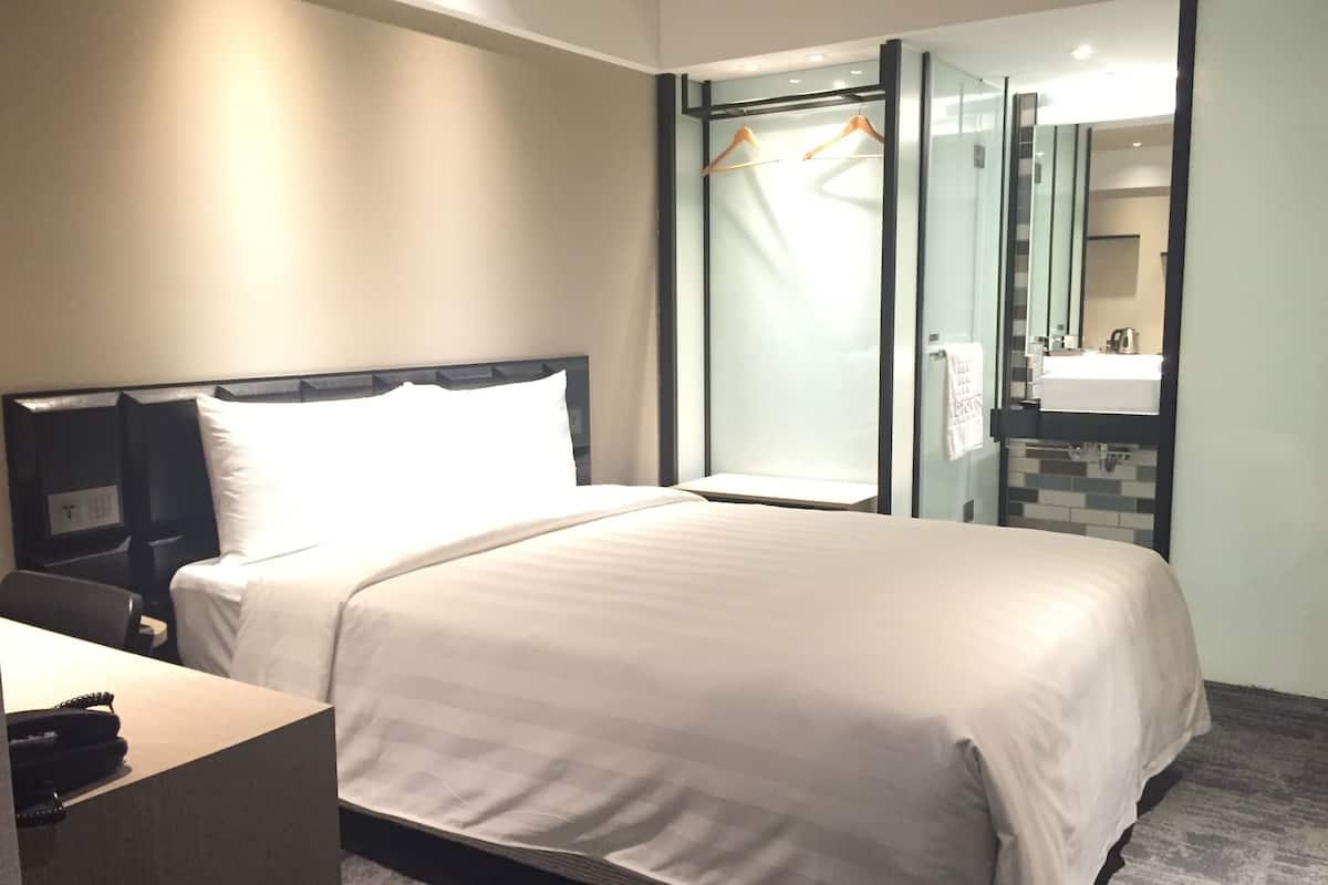 A hotel room with a bed, a desk, a mirror, and a bathroom with a sink and towel rack.