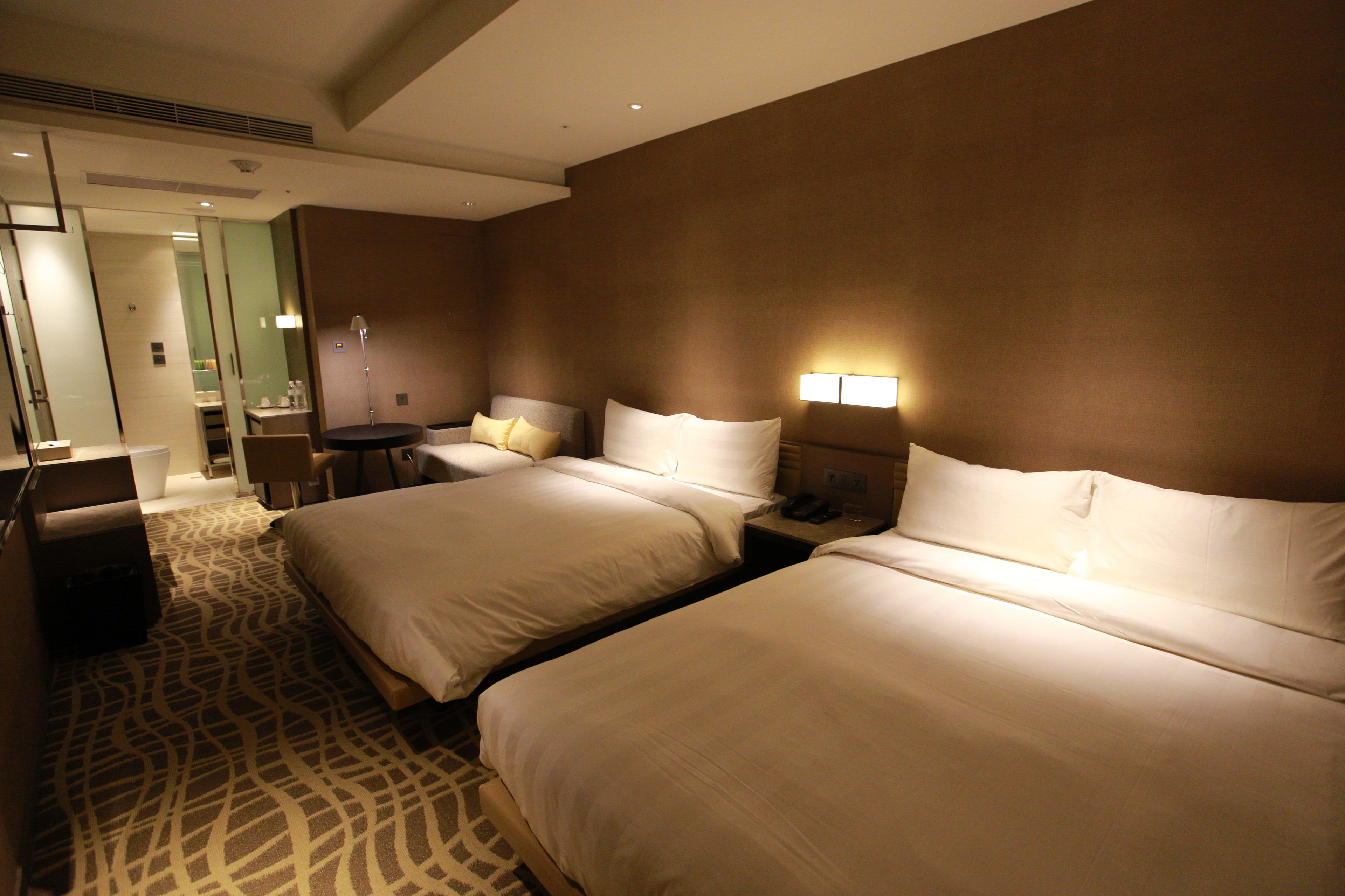 A hotel room with two beds, a desk, a chair, and a bathroom visible through an open door.