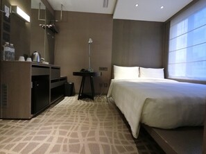 Una habitación de hotel con cama, escritorio con lámpara, espejo y minibar.