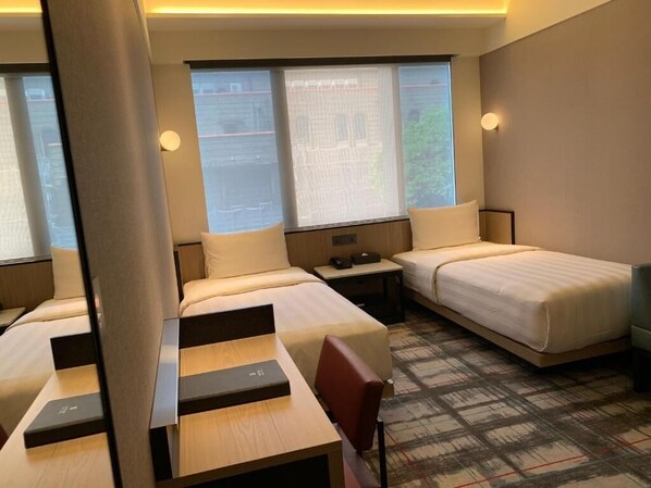 A hotel room with two beds, a desk, and a chair. There are windows with curtains, a nightstand, and a lamp. - Hotel Midtown Richardson (Taipei)