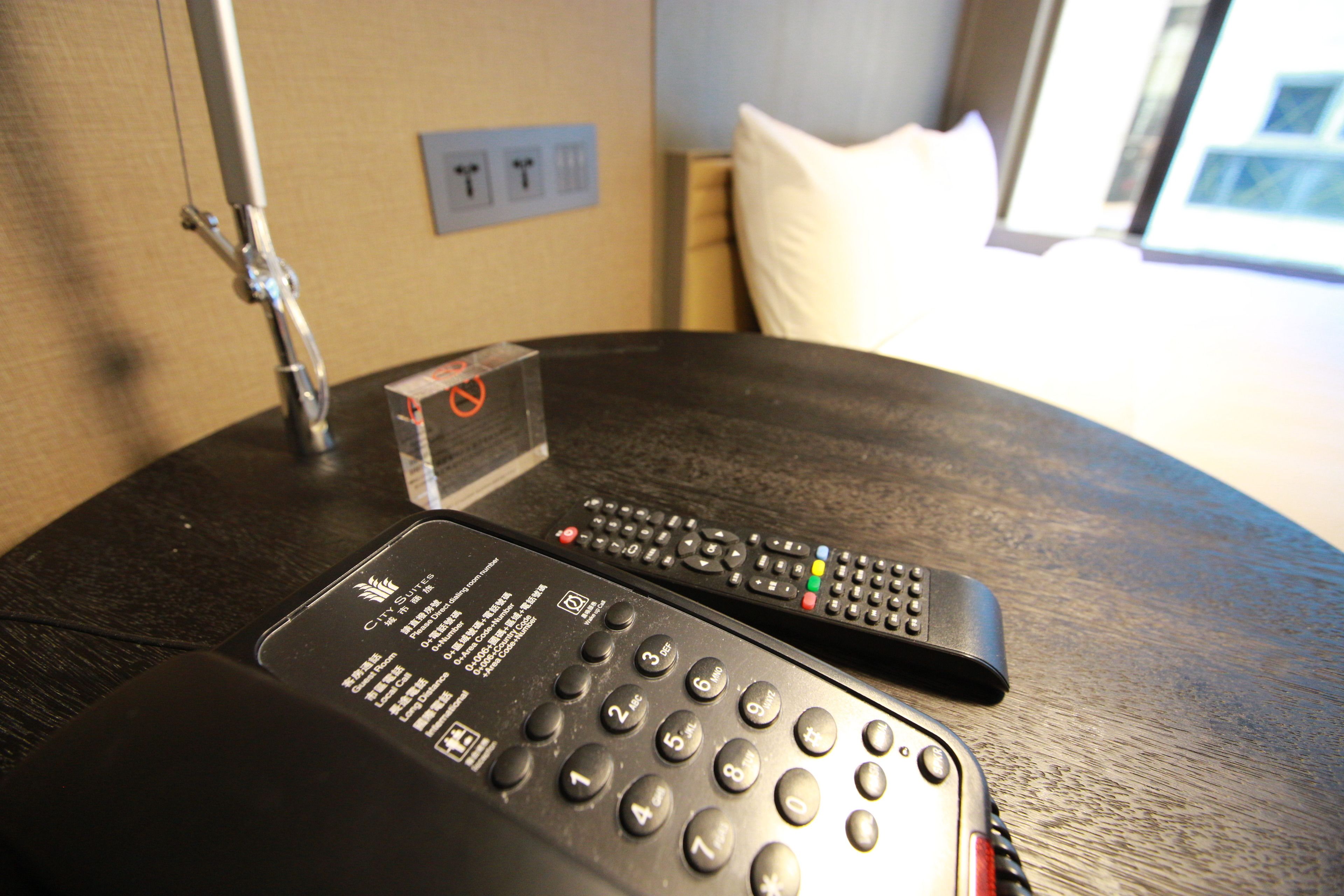 A hotel room with a round table, two remote controls, and a "no smoking" sign.