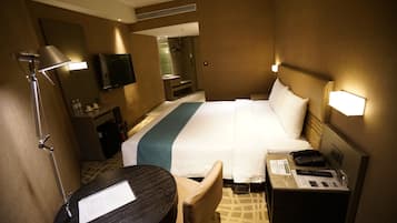 A hotel room with a bed, bedside table, lamp, TV, and a desk with a chair.