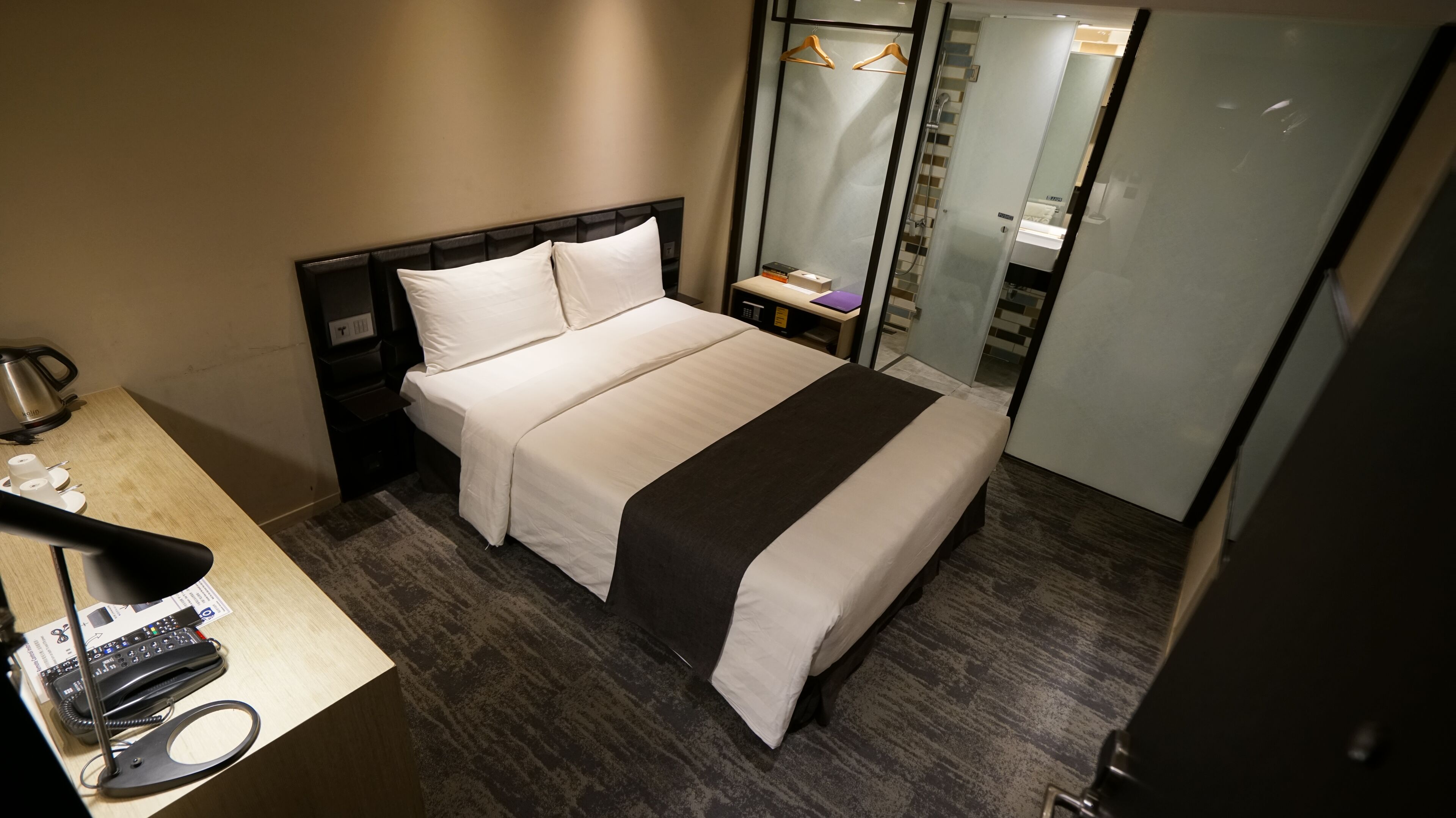 A hotel room with a bed, a bedside table with a telephone, a coffee maker, and a mirror.