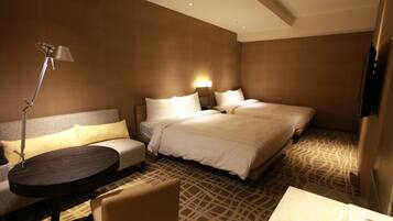 A hotel room with a sofa, two beds, a table, and a lamp.