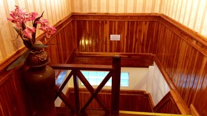 A wooden staircase with a railing, a vase with pink flowers, and a sign on the wall. - Apple Guesthouse (Luang Prabang)