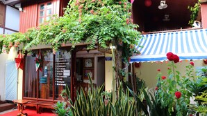 A traditional building with a red exterior, a wooden bench outside, and a variety of plants and flowers. - Apple Guesthouse (Luang Prabang)