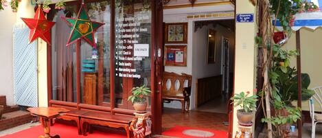 A hotel entrance with a red carpet, wooden furniture, and potted plants.