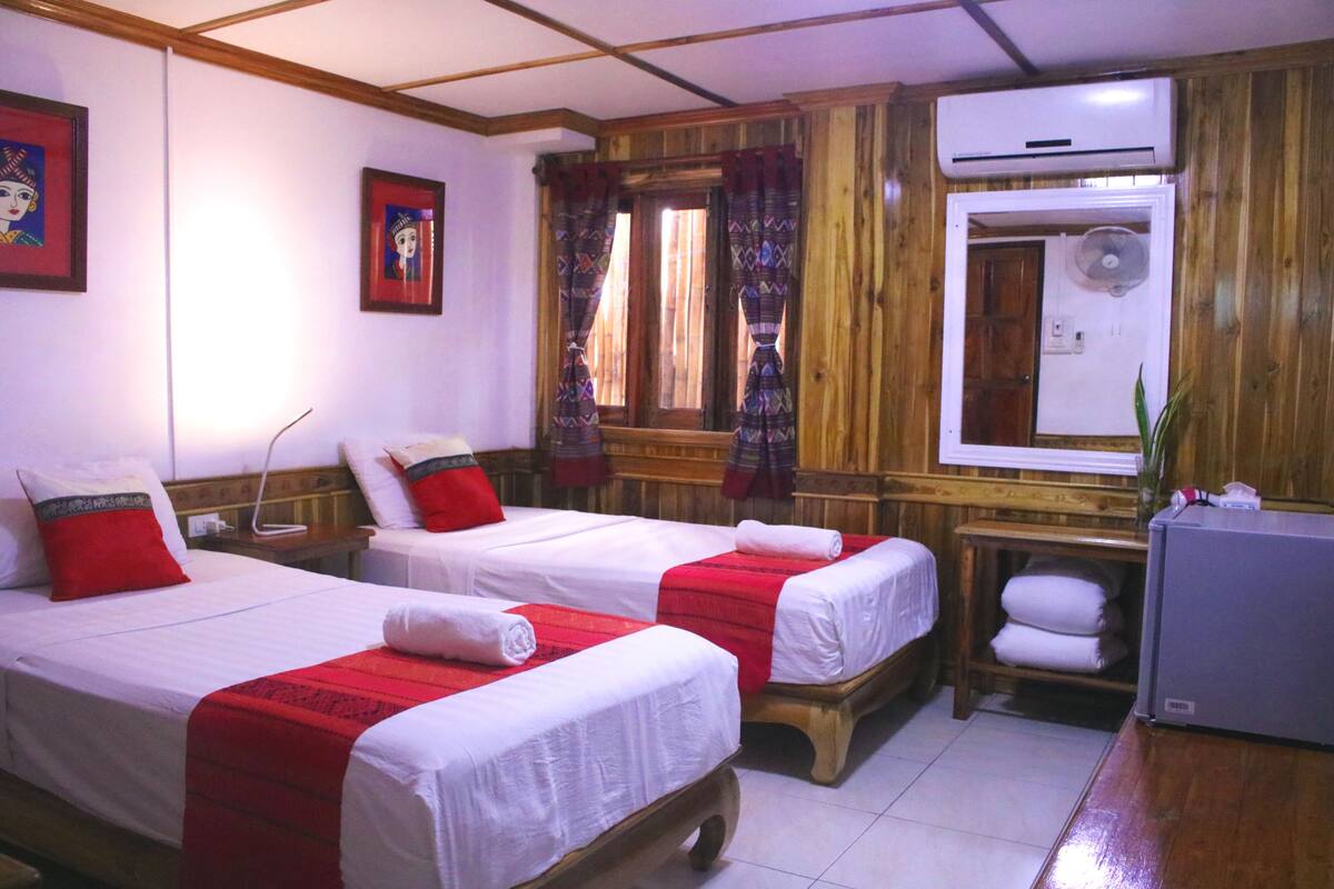 Una habitación de hotel con dos camas individuales, un armario de madera, un equipo de aire acondicionado y un refrigerador pequeño.
