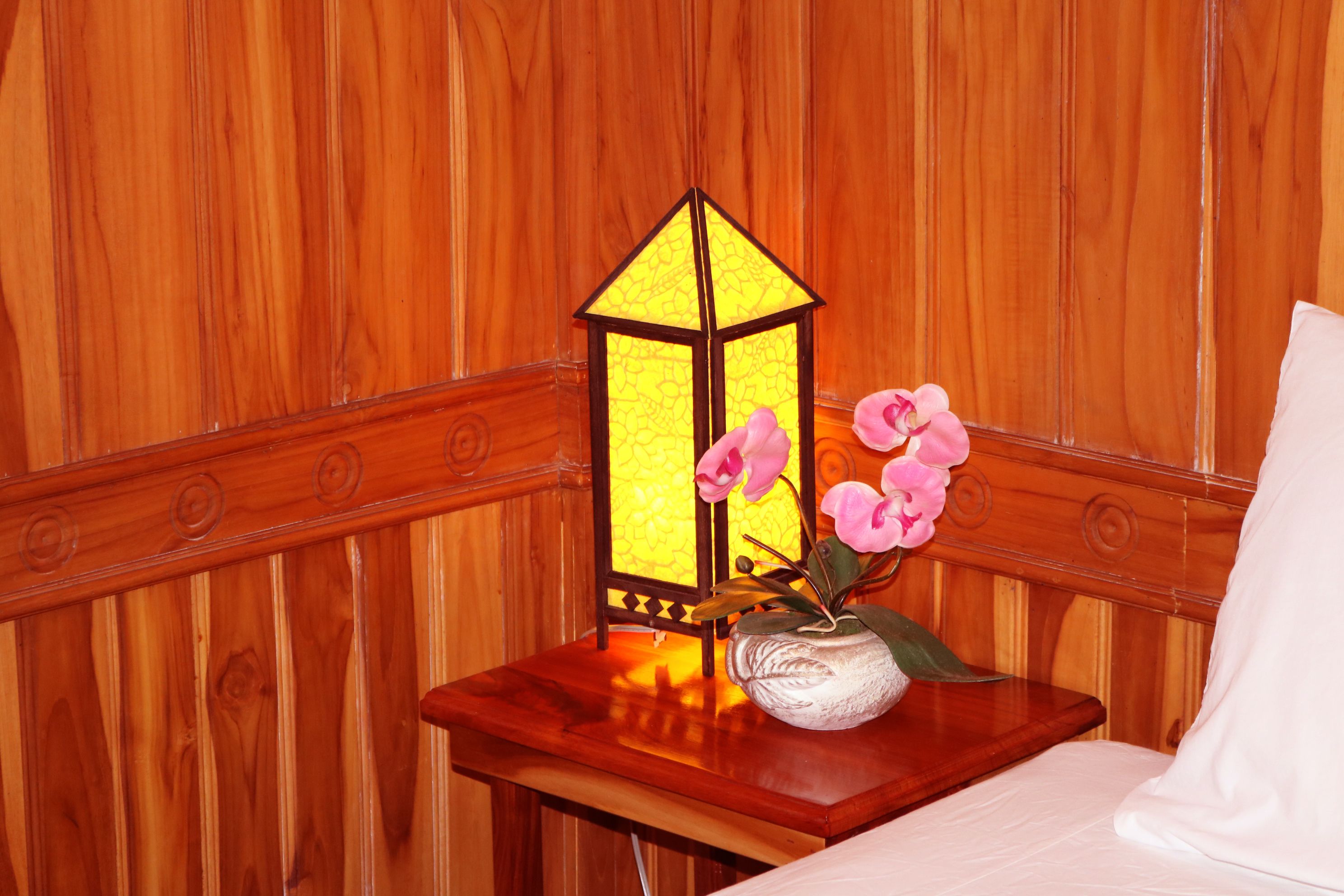 Pared de madera con un banco de madera y una pequeña mesa con un jarrón de flores rosas y un farol.