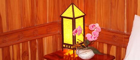Pared de madera con un banco de madera y una pequeña mesa con un jarrón de flores rosas y un farol.