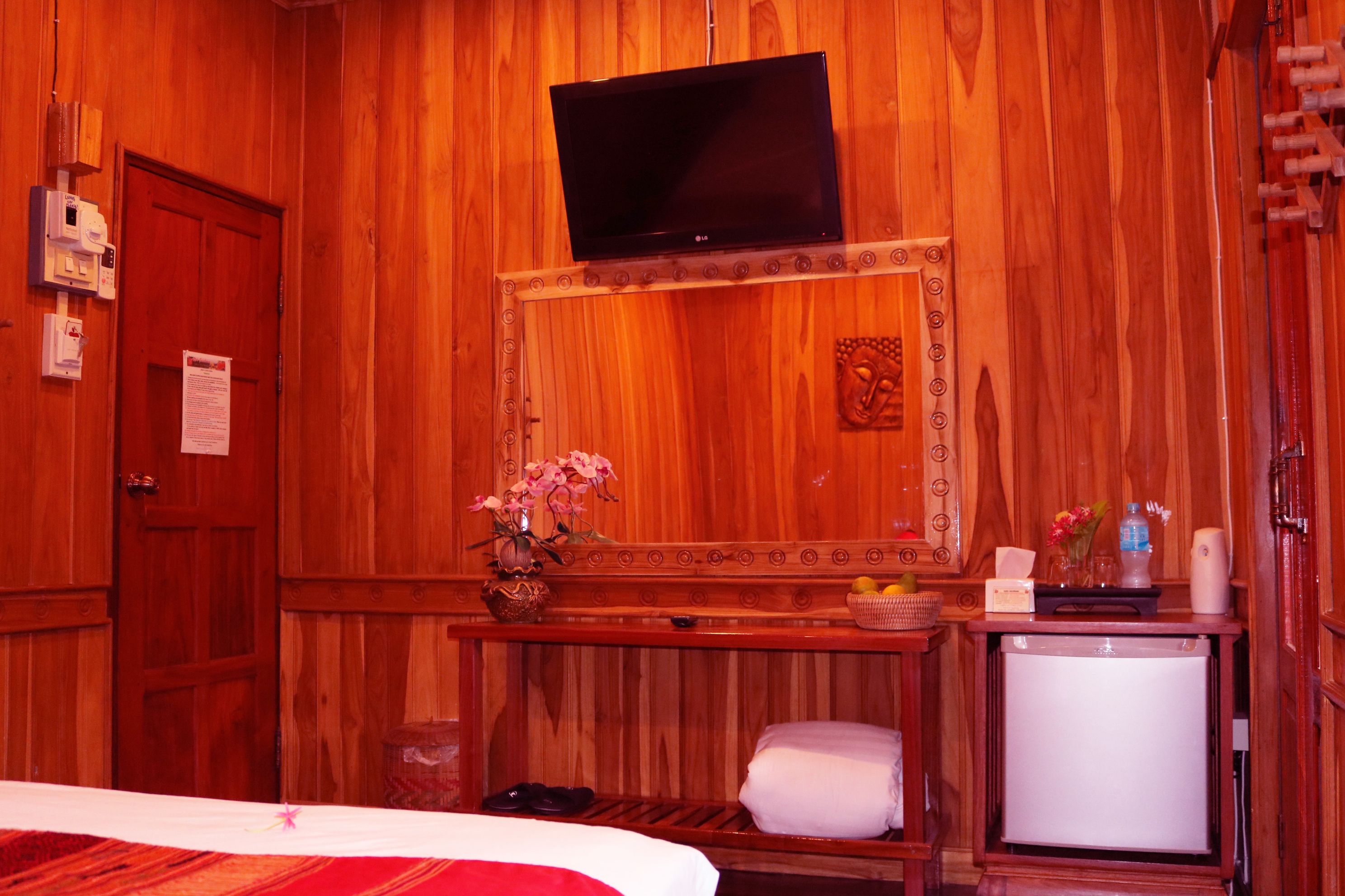 Una stanza in legno con una televisione a parete, un tavolino con un vaso di fiori e un frigorifero.