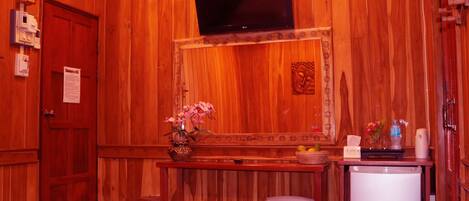 Una stanza in legno con una televisione a parete, un tavolino con un vaso di fiori e un frigorifero.