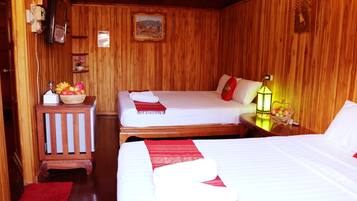 A wooden room with two beds, a small table with fruit, a red rug, and a wall-mounted TV.